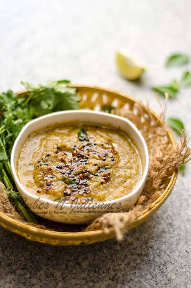 Dosakaya Chutney in a white bowl, some coriander leaves, lemon and curry leaves at the back.