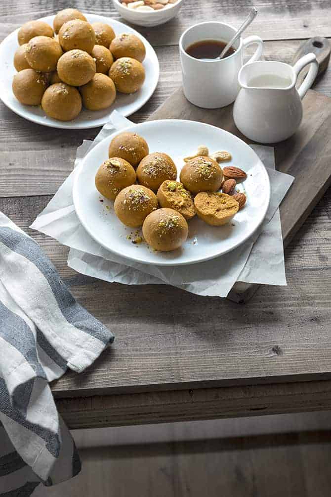 Besan ladoo sweet served on two white plates, coffee and milk pot on the side