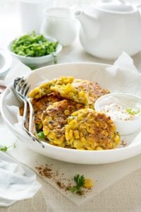 Corn fritters served with dip on white plate.