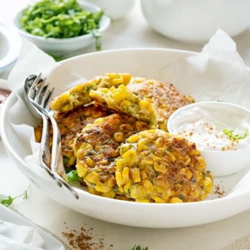 Corn fritters served with dip on white plate.