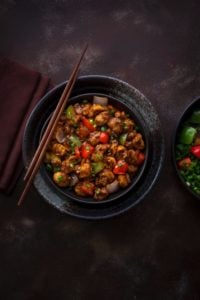 Indo Chinese vegan Mushroom Manchurian served in black bowl with a pair of chopsticks in it.