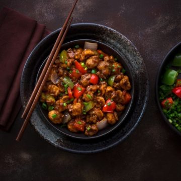 Indo Chinese vegan Mushroom Manchurian served in black bowl with a pair of chopsticks in it.