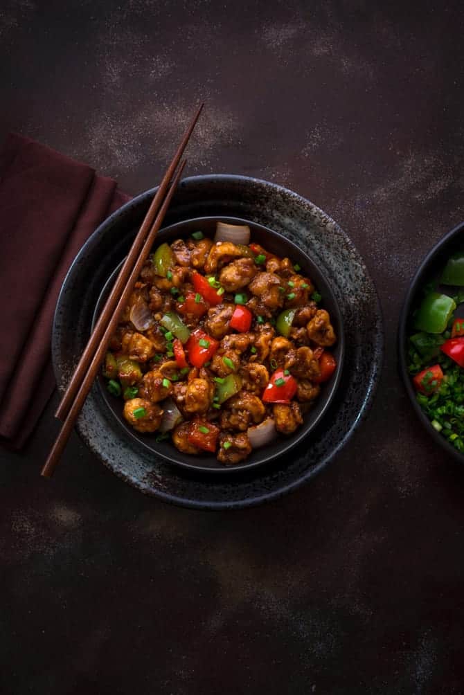 Crispy Vegan Indo Chinese Mushroom Manchurian served in black bowl with pair of chopsticks in it.