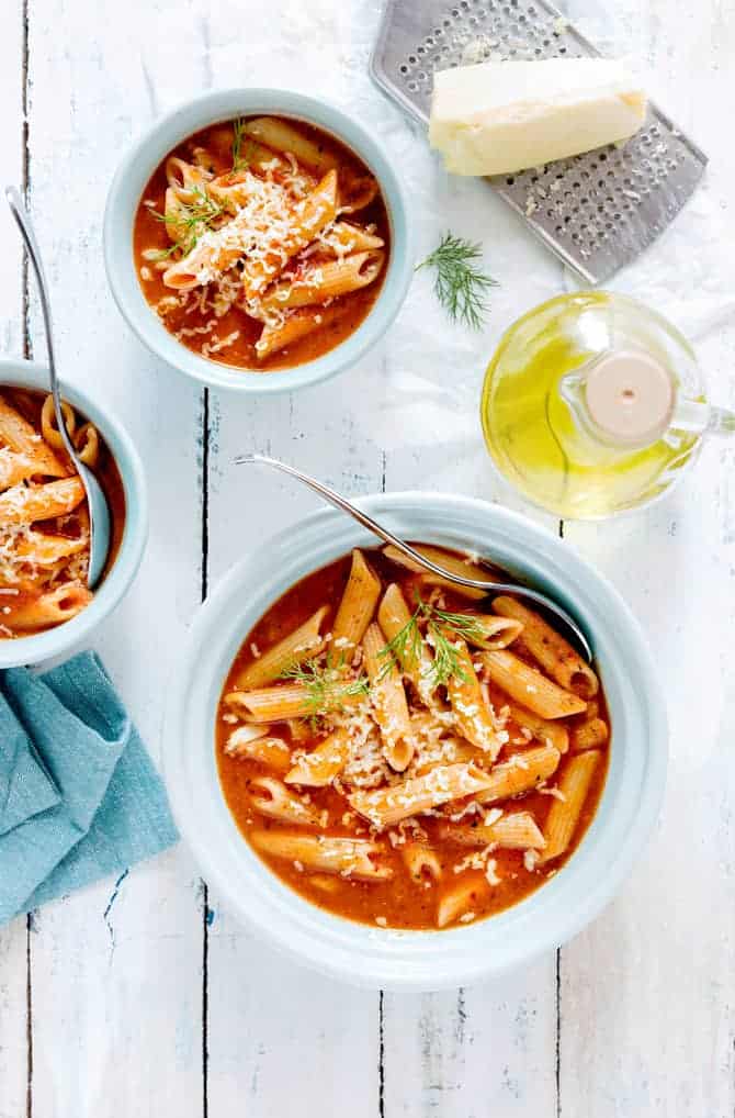 instant pot pasta soup with tomato served in 3 blue bowls with cheese on the side.