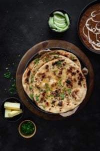 Tawa Garlic Naan on black plate with butter, salad and dal makhani on the side