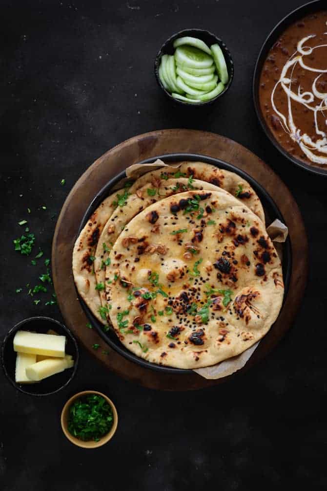 Whole wheat garlic butter naan on black plate with butter sticks, salad and dal makhani on the side