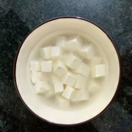 Paneer cubes soaked in hot water in bowl.