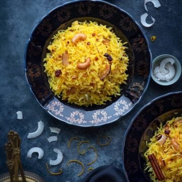 An over head shot of zarda served in served in a two blue plates, coconut slices and orange zest in a small bowl and around