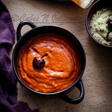 Spicy tangy Onion tomato chutney in a black bowl, dosa and white coconut chutney on the side