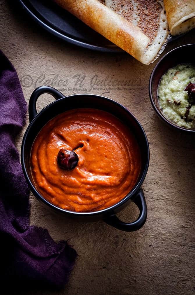 Spicy tangy Onion tomato chutney in a black bowl, dosa on the side.