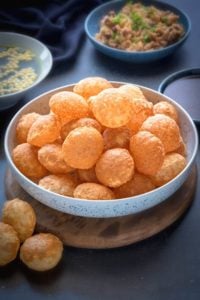 Crisp puffed Golgappa Puri for pani puri in a large bowl. Golgappa pani, its filling and sweet chutney in abowl at the back.