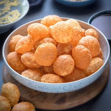 Crisp puffed Golgappa Puri for pani puri in a large bowl. Golgappa pani, its filling and sweet chutney in abowl at the back.