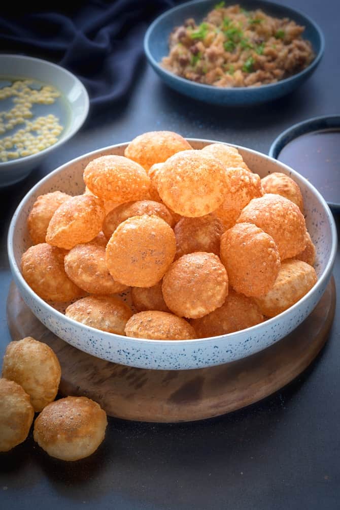 Puffed Golgappa Puri for pani puri in large bowl. Golgappa pani, filling and sweet chutney at the back.