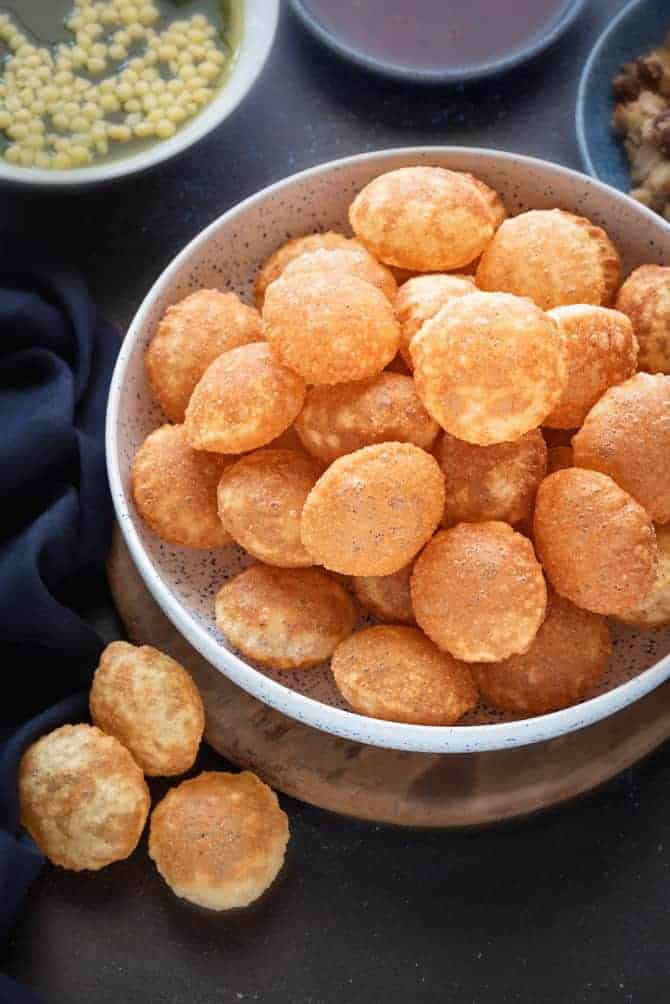 Crisp Fried puffed golgappa puri (pani puri) served in a large bowl. Golgappa pani, filling and sweet chutney on the side.