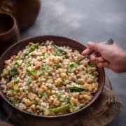 Kid's hand holding a spoon kept in sabudana khichdi which is served in a wooden bowl.