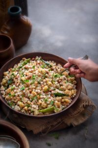 Kid's hand holding a spoon kept in sabudana khichdi which is served in a wooden bowl.