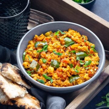 Close up shot of Paneer Bhurji served in blue bowl with naan bread on the side.