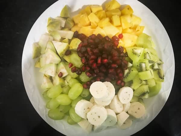 assorted cut fruits on white plate for the making of fruit chaat recipe.