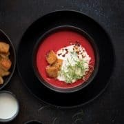 Overhead shot of beetroot tomato soup in lack bowl with croutons on the side
