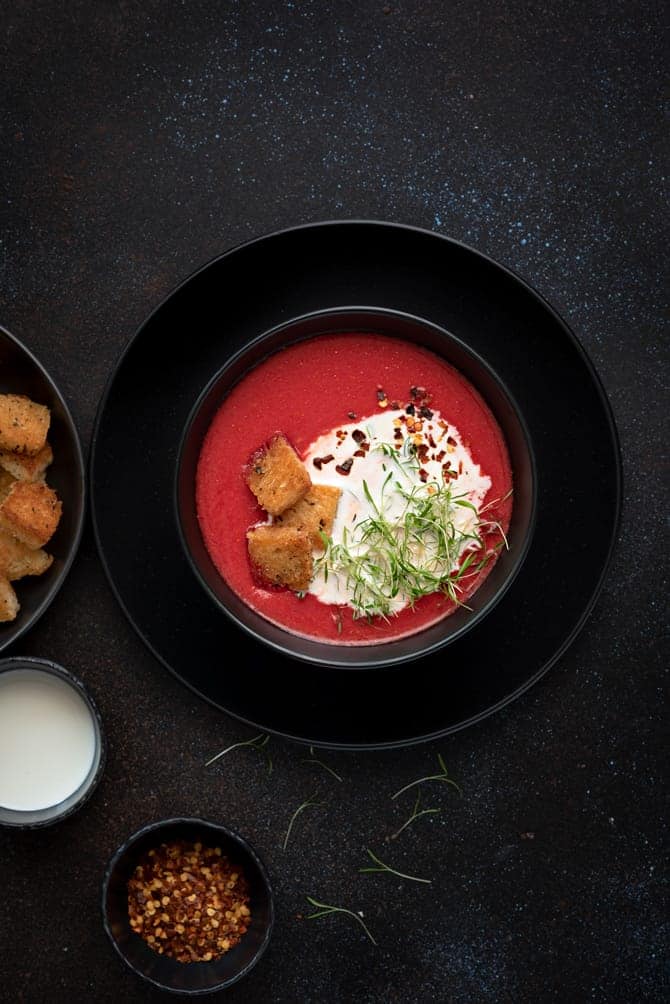 Overhead shot of beetroot tomato soup in lack bowl with croutons on the side