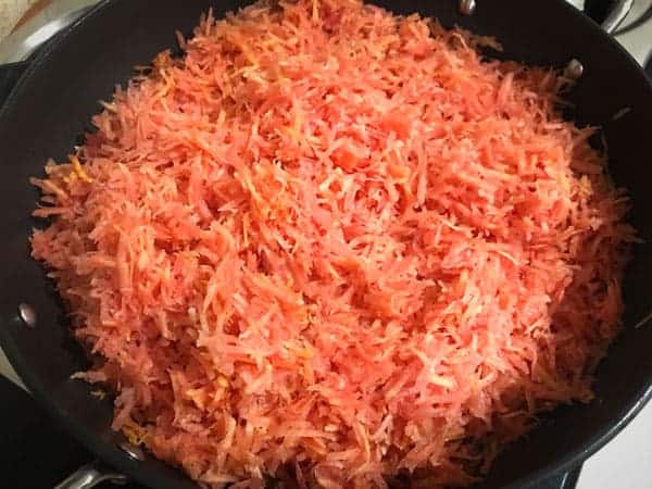 Grated red carrots added in hot ghee in a pan.