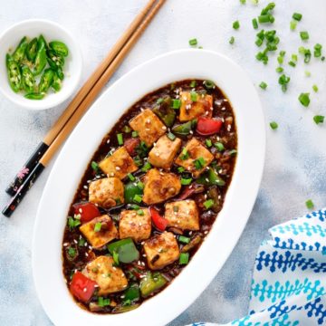 Spicy Chilli Paneer gravy erved in a white oval plate with a pair of chopsticks