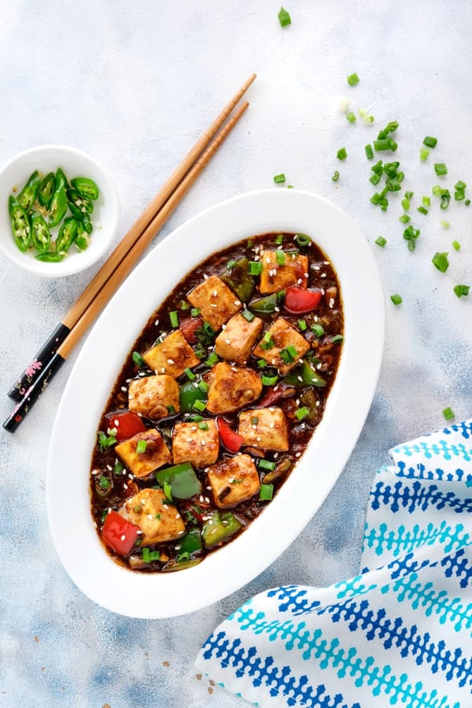 Spicy Chilli Paneer gravy served in a white oval plate with a pair of chopsticks