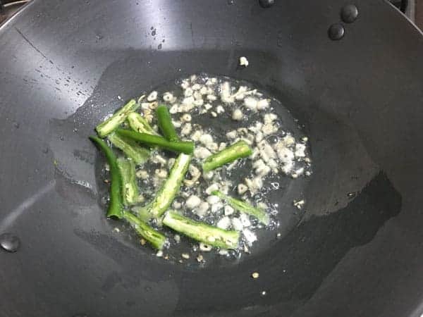 Garlic and green chilies added in hot oil in a wok.
