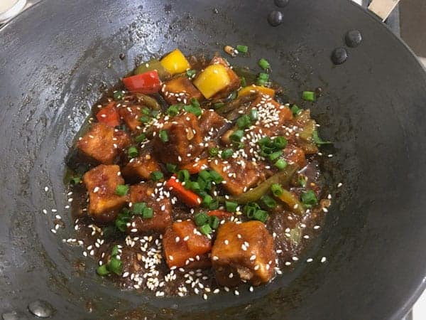 Sesame seeds, spring onions added in a wok to finish the Chilli Paneer dish.