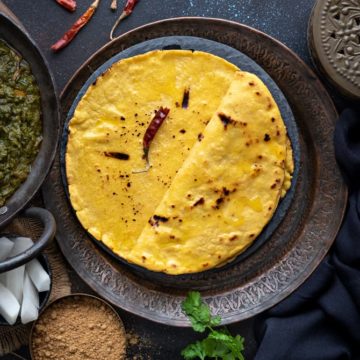 Punjabi Makki Ki Roti topped with ghee and served on a traditional plate with jaggery, radish and saag on the side