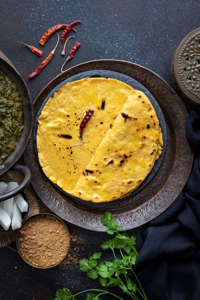 Punjabi Makki Ki Roti topped with ghee and served on a traditional plate with jaggery, radish and saag on the side