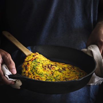 A pair of hands holding an iron pan with moong dal chilla in it.