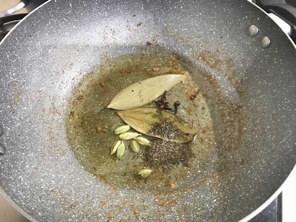 Bay leaves, green cardamom, cloves and shajeera added in hot oil in pan