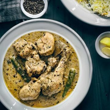 Overhead shot of chicken kali mirch in white plate with pulao the side.