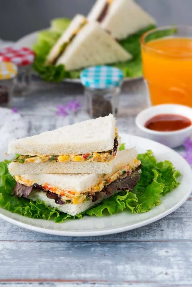 A stack of cold cream cheese sandwich served on white plate, glass of juice on the side.