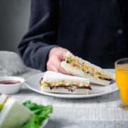 A baby hand holding veg cream cheese sandwich, glass of juice on the side.