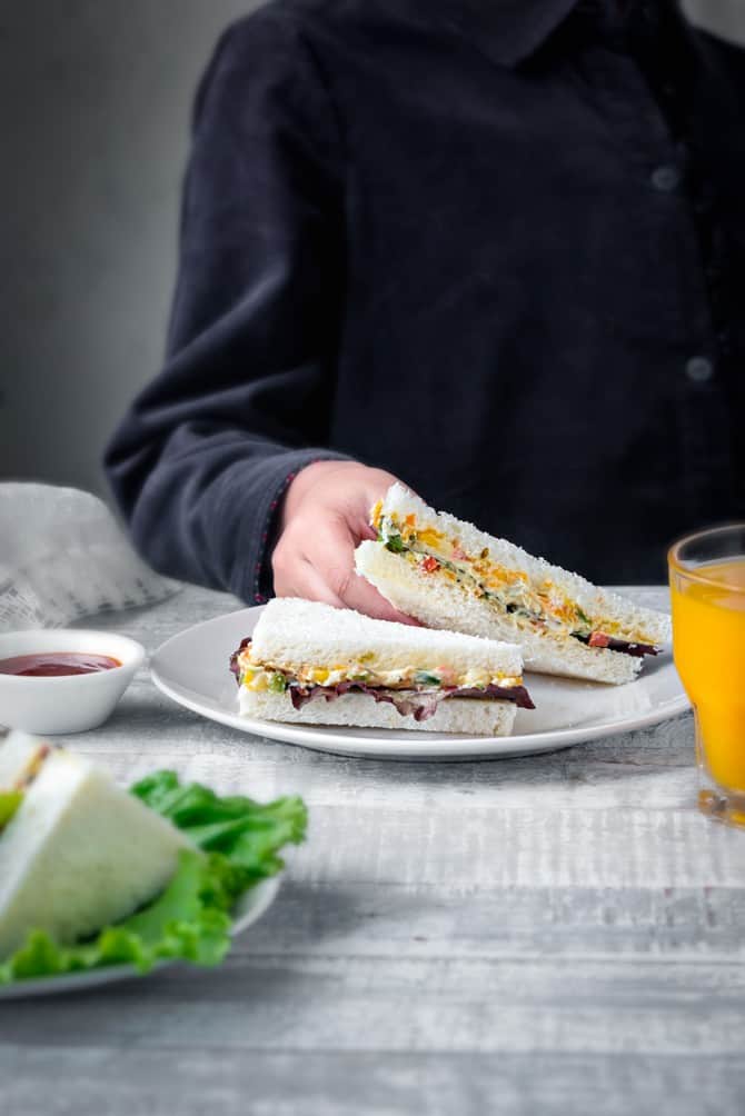 A baby hand holding veg cream cheese sandwich, glass of juice on the side.