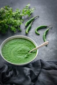 Spicy Green Chutney in small bowl with coriander and chilli at the back