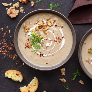 Creamy Cauliflower soup served in two brown ceramic bowls with croutons on the side