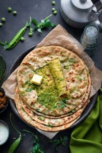 Overhead shot of spicy Matar paratha on black plate with top paratha cut open to show the peas filling.