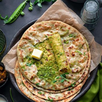 Overhead shot of spicy Matar paratha on black plate with top paratha cut open to show the peas filling.