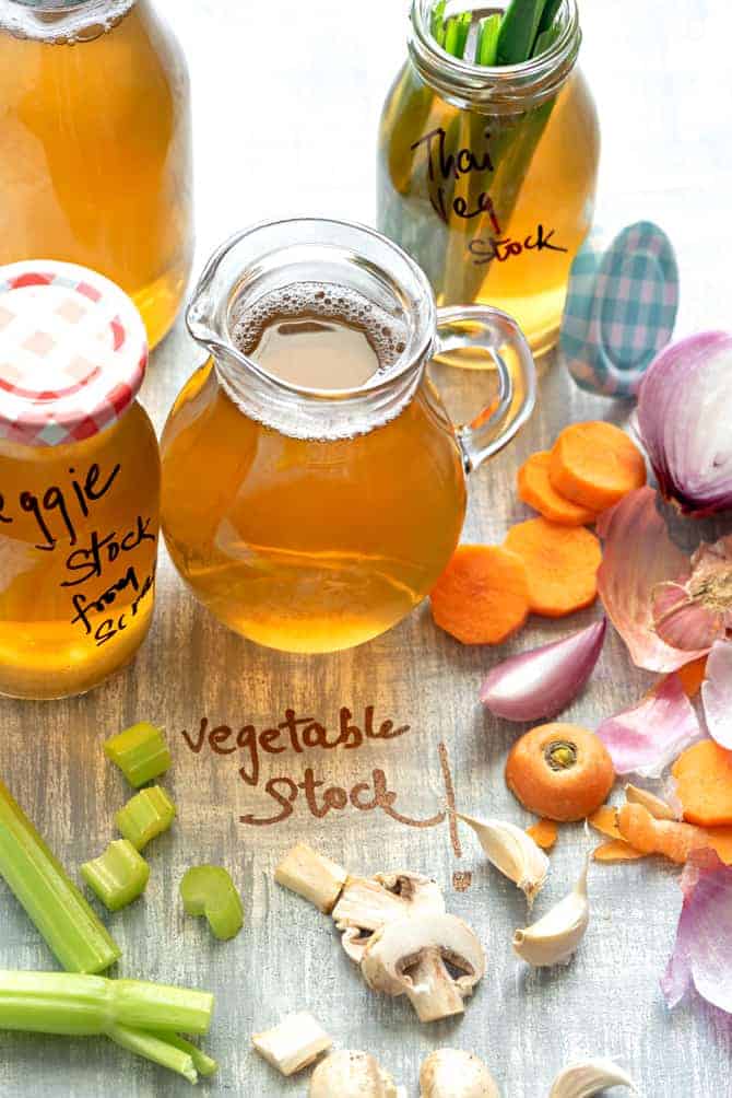 Vegetable Broth in glass pitcher and bottles along with some veggies spread around
