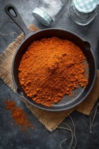 Homemade achari masala powder in cast iron pan with glass jars on the side.