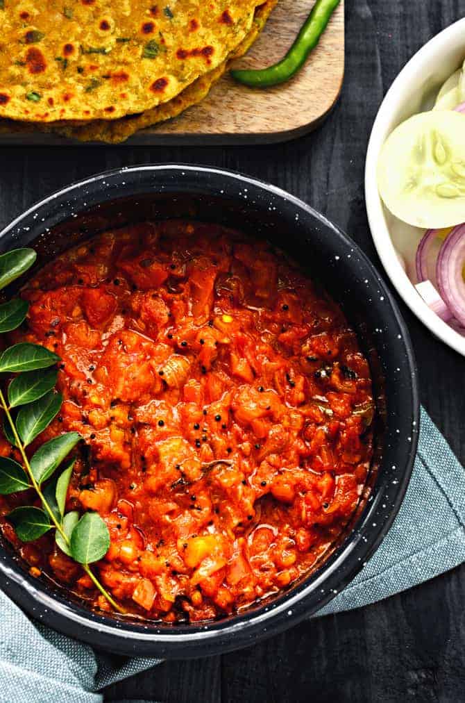 Close up shot of Tomato Chutney in pan with a sprig of fresh curry leaves in it.