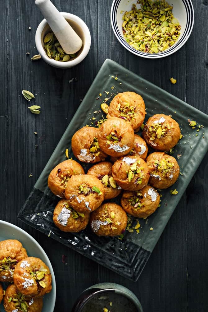 Overhead shot of Balushahi on rectangular plate with a small pistachio bowl on side.