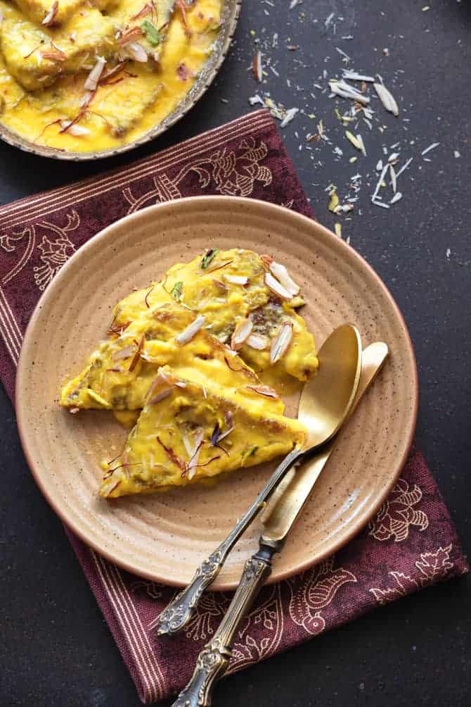 Overhead shot of Hyderabadi Shahi Tukra served in brown plate with pair of spoon and knife.