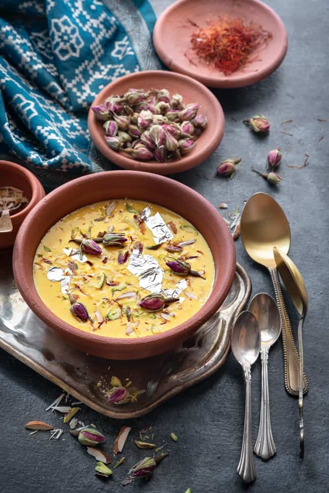 Garnished Rabdi served in an earthen pot, few rose buds and saffron at the back.