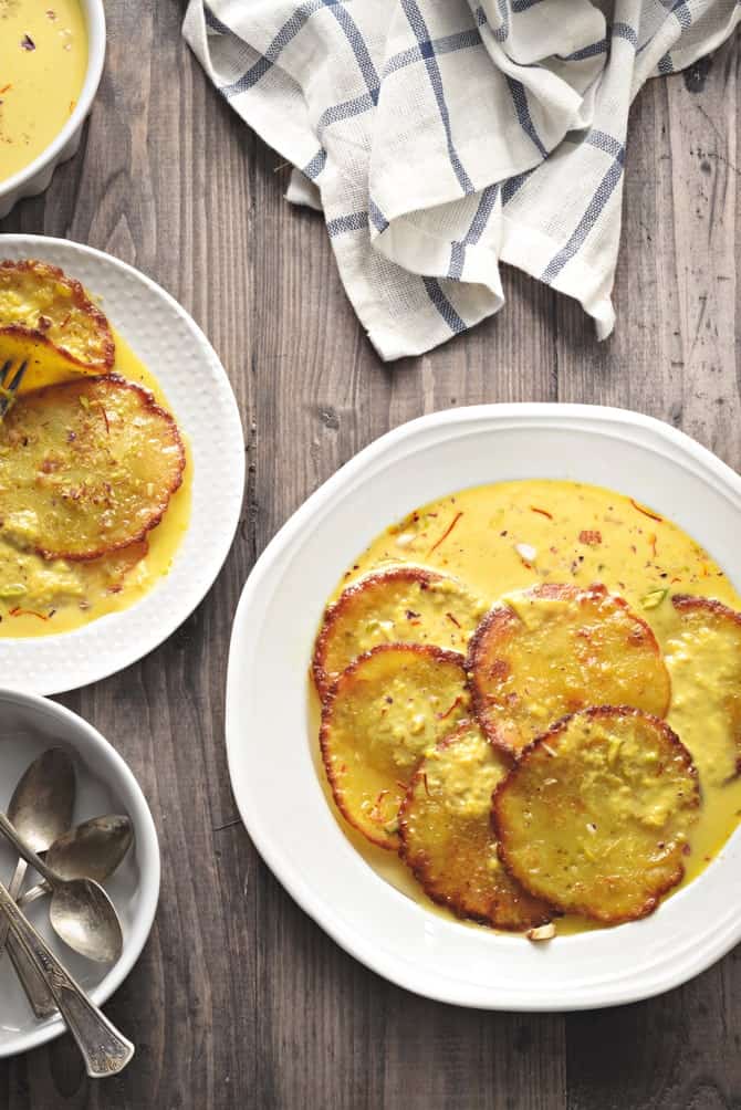 Overhead shot of Malpua rabdi served in white plate, few spoons on the side.