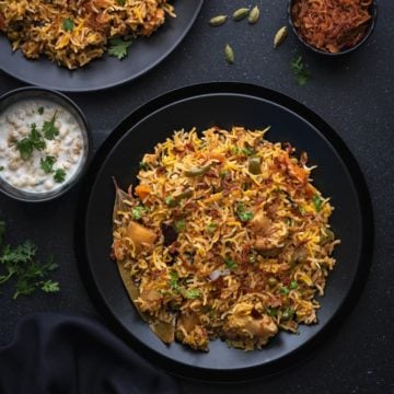 Instant pot vegetable biryani served in 2 black plates with Indian raita on side.