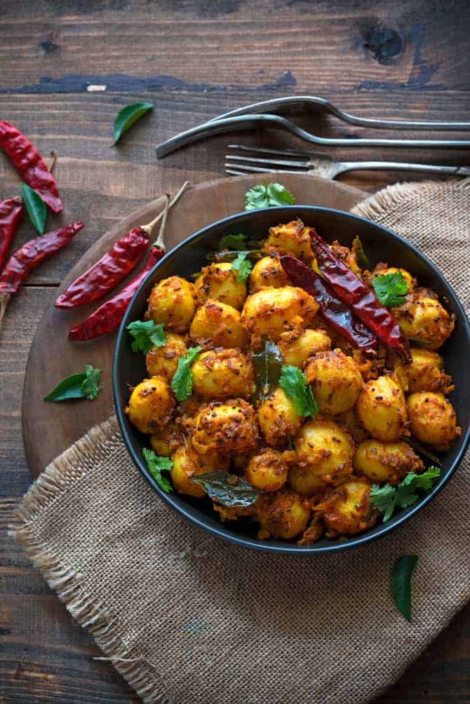 Spicy masala roast baby potatoes fry served on black plate with dried chilies spread around